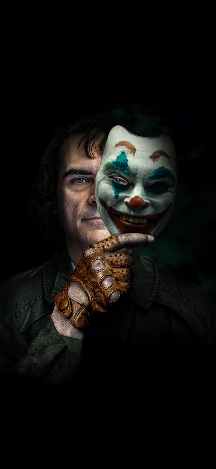 A clown mask is held in hand on a dark background