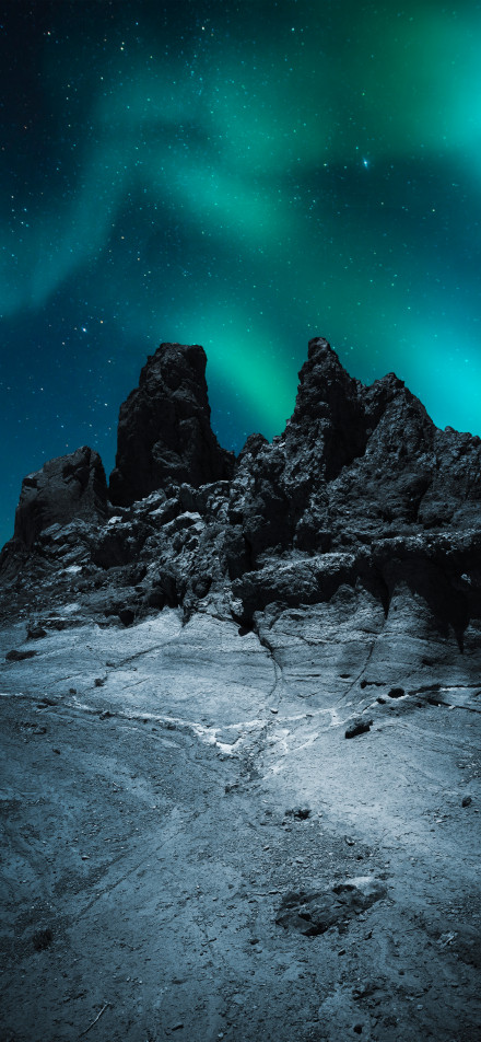 Green aurora dancing in the night sky above the rocks phone wallpaper